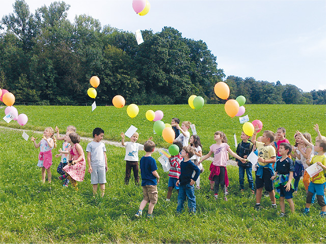 Kinder lassen auf einer Wiese Ballone fliegen.